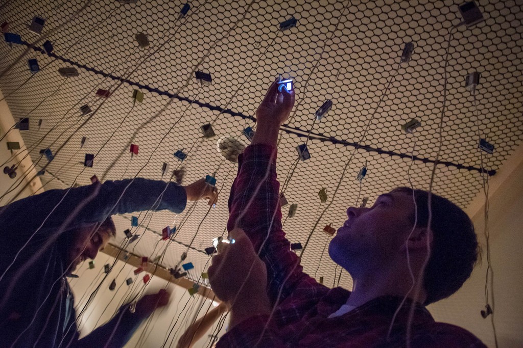 Students reach for one of several earbuds and ipods suspended above.