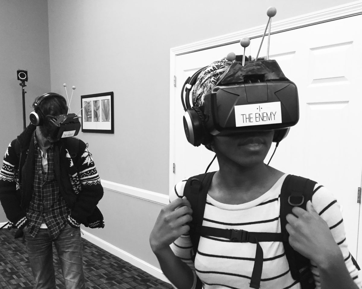 A participant in The Enemy wears a VR headset and holds onto the straps of a backpack containing equipment.