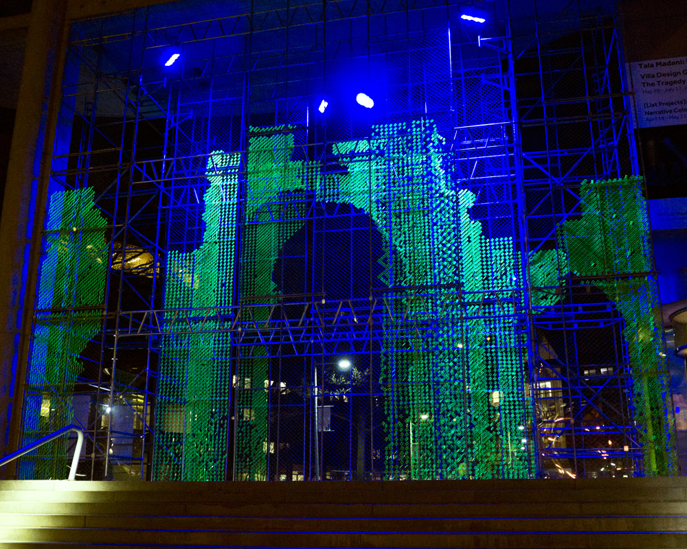 A large green arch surrounding by blue scaffolding illuminated at night.