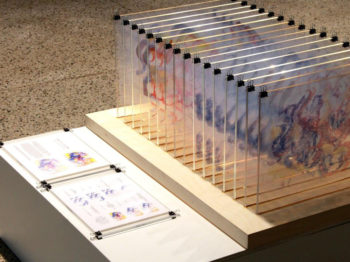 A series of glass plates with watercolor paintings are lined up in a row.