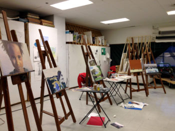 Four easels with oil paintings in an art studio.