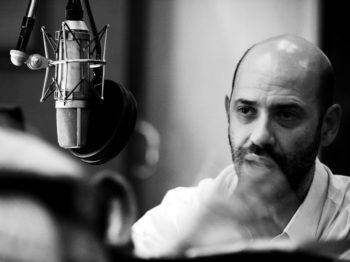 A black and white photo of Guillermo Klein behind a microphone.
