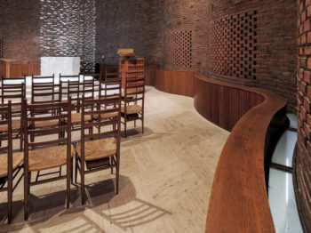 An undulating brick wall, chairs, and a view of the altar in the MIT chapel.