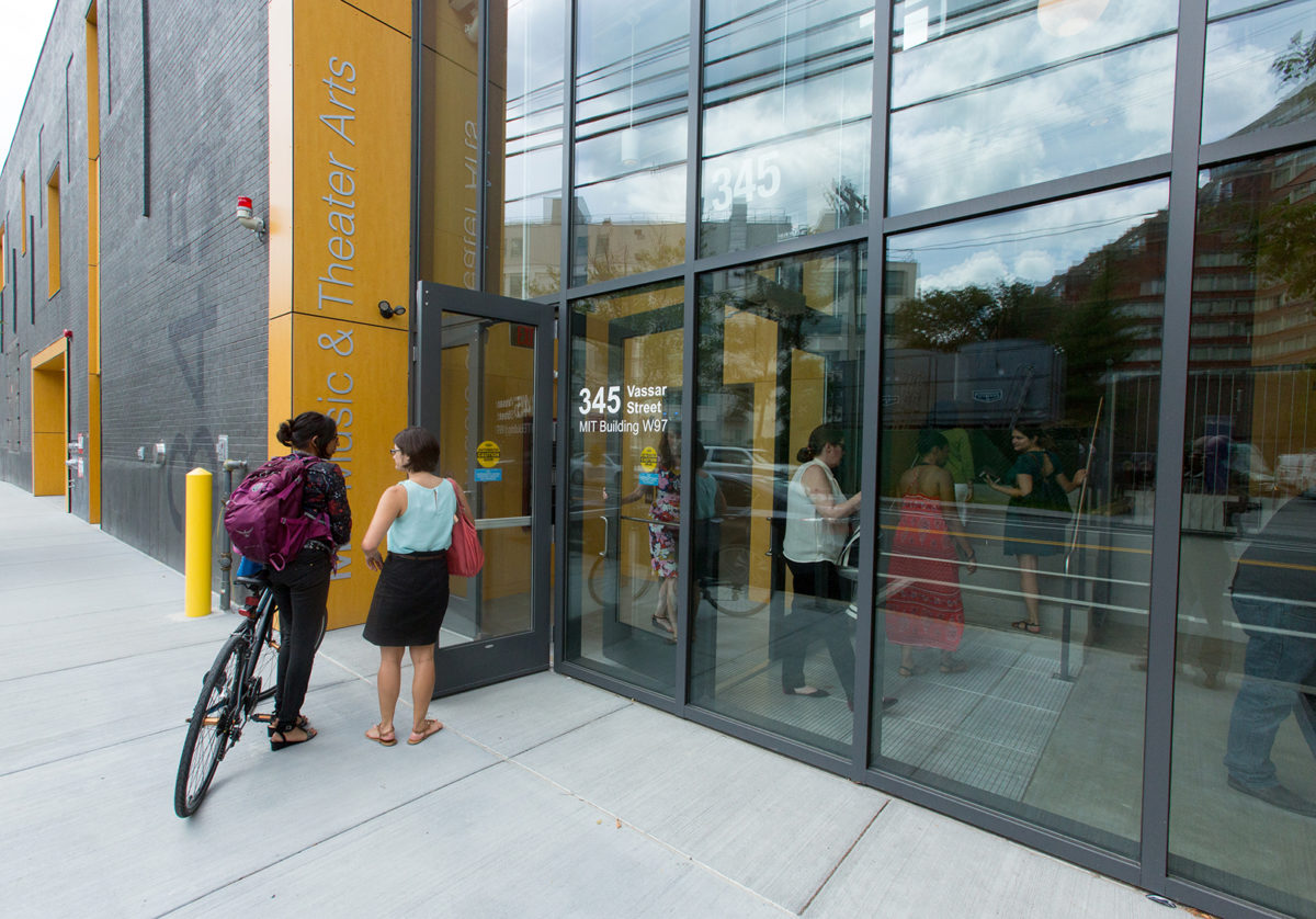 Two students enter a yellow and grey building.