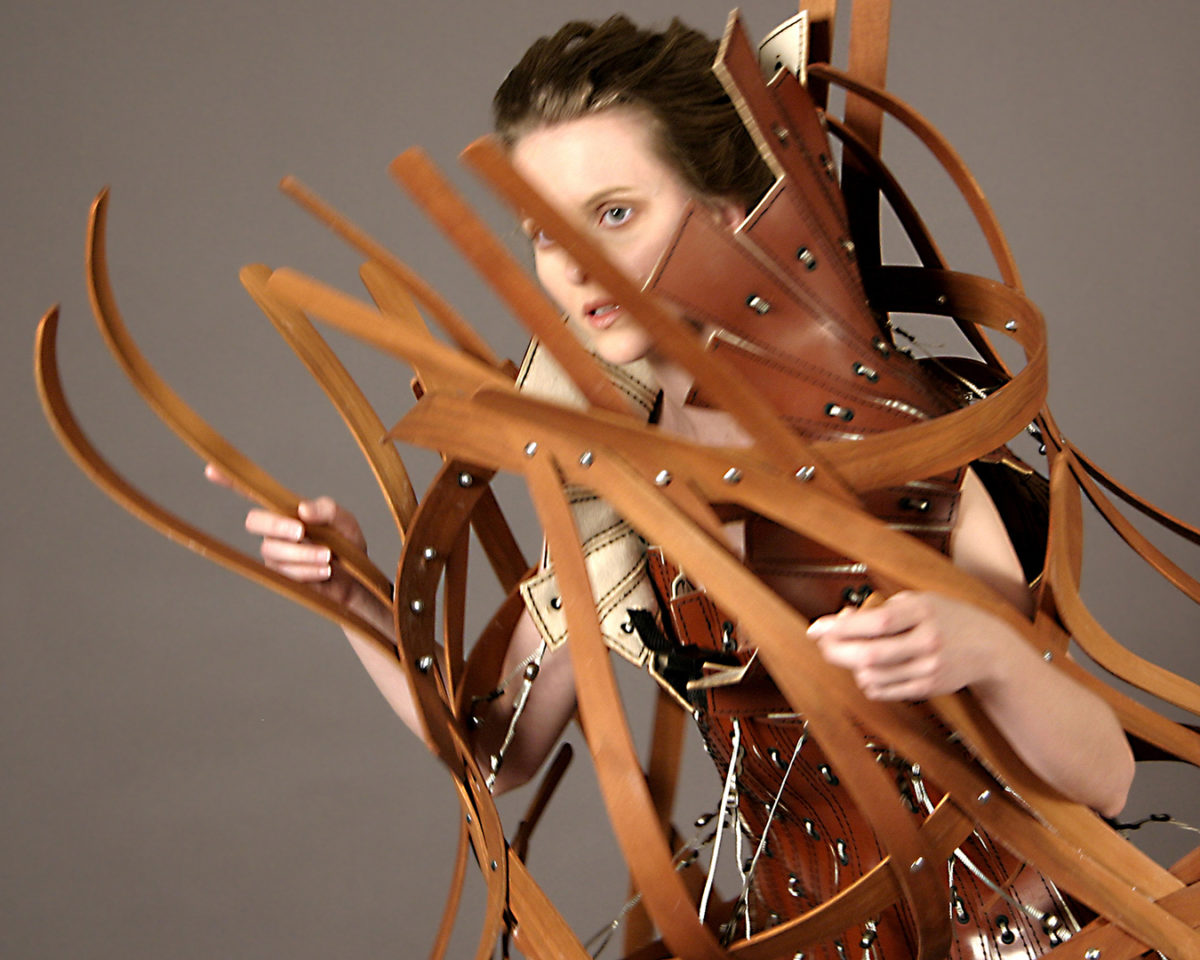 A woman wears a complex structure of thin wood pieces.