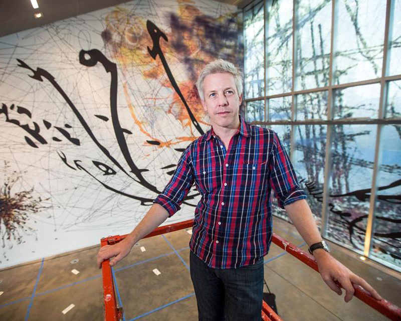Artist standing in front of a large wall painting.