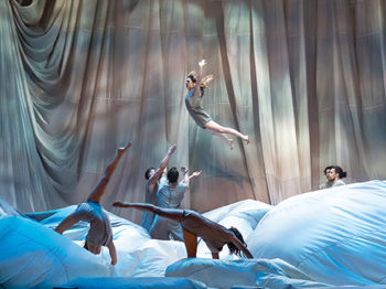 Artists perform acrobatics on a set of flowing cloths and dappled light.