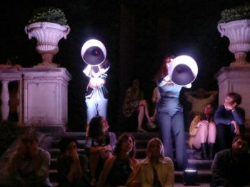 Singers with megaphones are illuminated on a stone staircase.