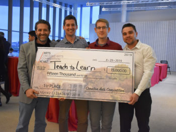 Four men pose with a large check reading "Teach to Learn."