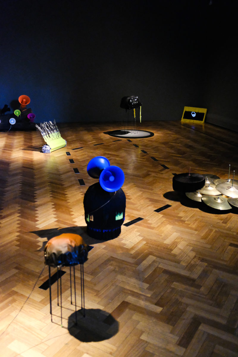 Installation view of multicolored sonic sculptures on a hardwood floor.