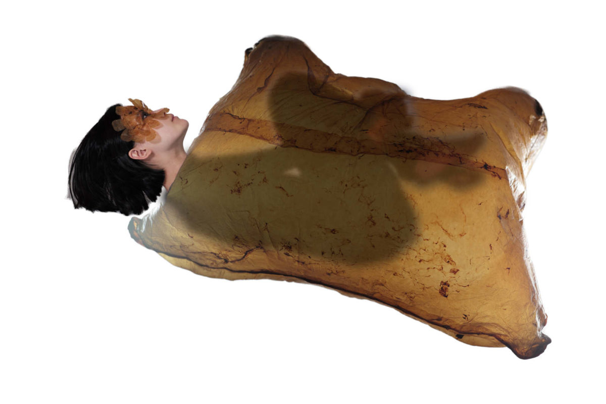 A figure lays on a white floor inside an inflatable scoby.