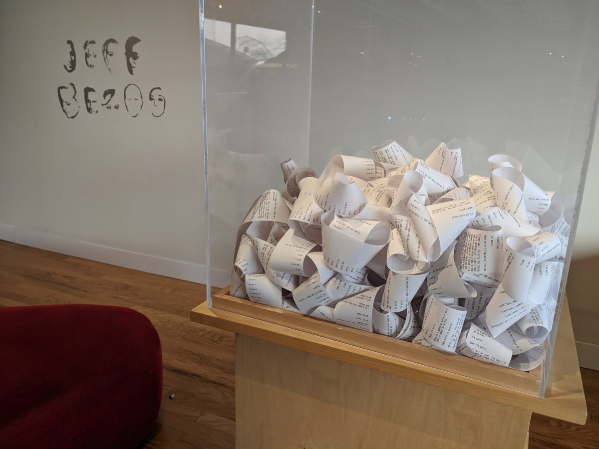 Installation view of "Box of Apologies" with rolls of receipt paper inside of a glass vitrine on a pedestal.