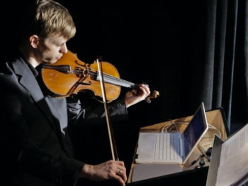 Christian Frederickson plays the viola while looking at a laptop.