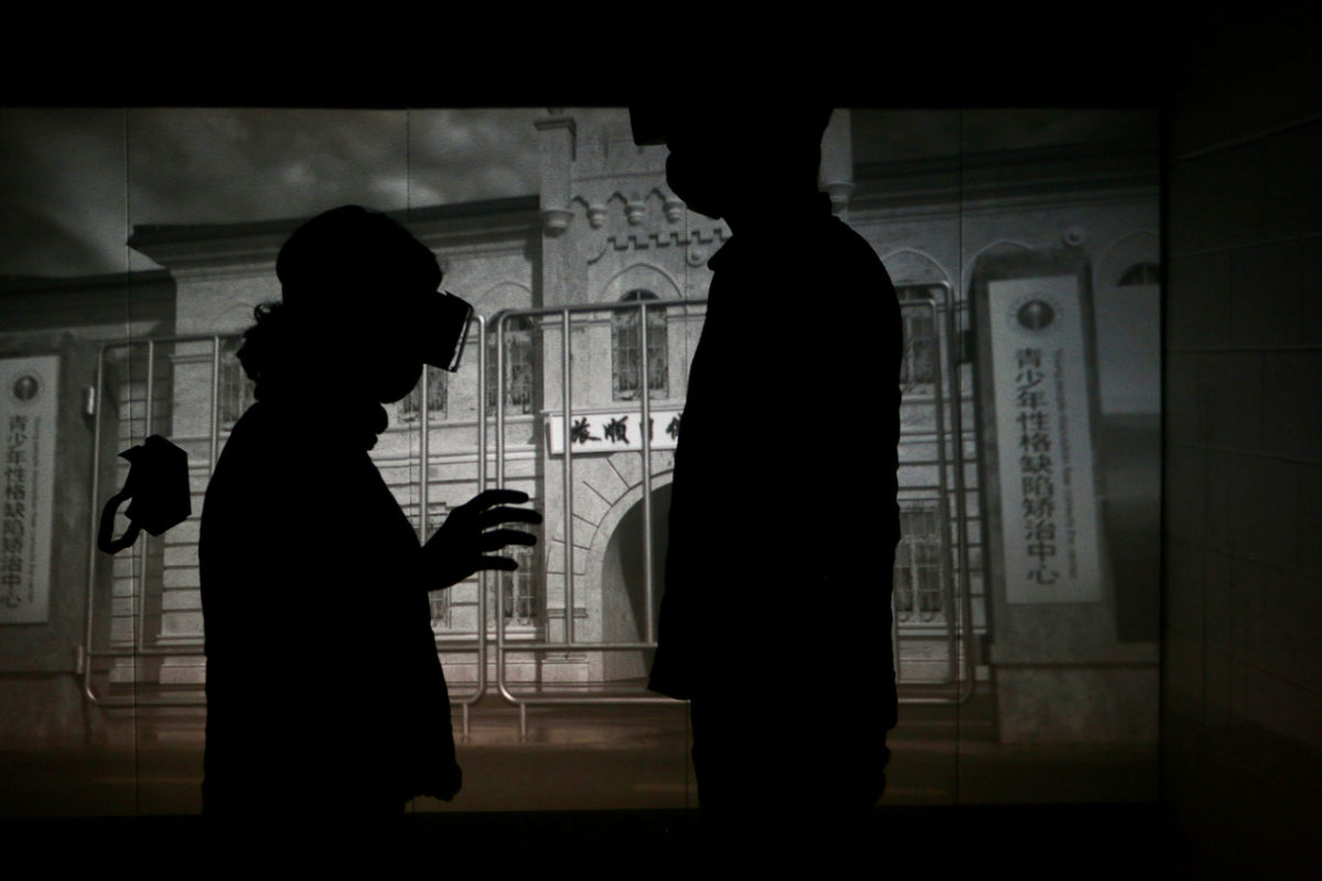 Two participants wearing cardboard VR headsets stand in front of a projected image of a building.