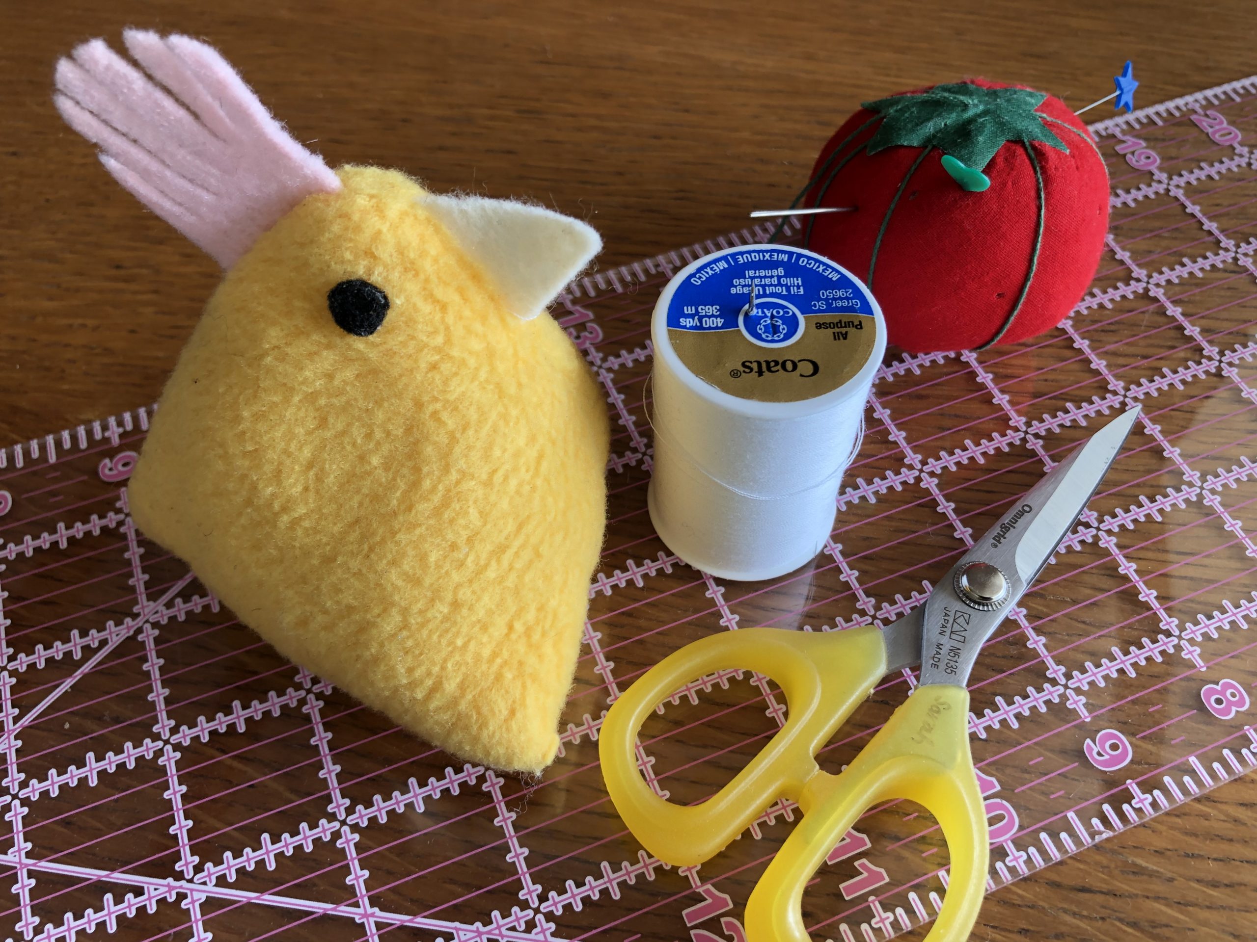 Stuffed animal, thread, scissors, and pincushion on a cutting mat.
