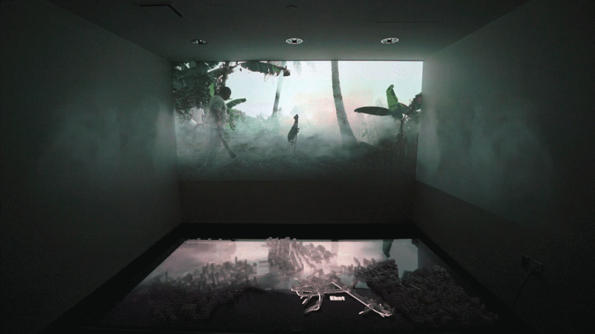 A dark room is filled with mist as a video of a jungle plays on the back wall.