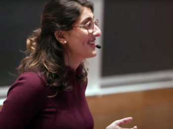 Profile view of Talia Khan speaking to an audience while wearing a headset microphone.