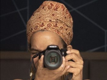 Woman holds camera, she is wearting a brown headscarf