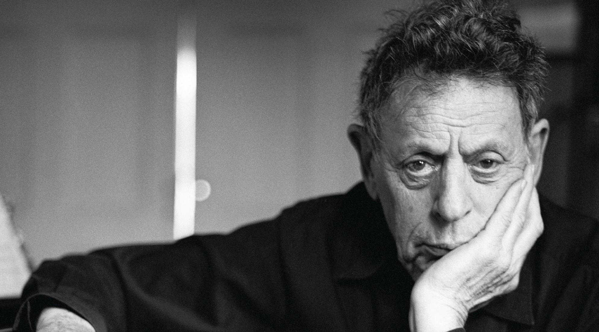 Philip Glass looking into the camera with a stern look.