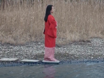 Pianist Maki Namekawa wearing a red and pink kimono by a river on a cloudy day.