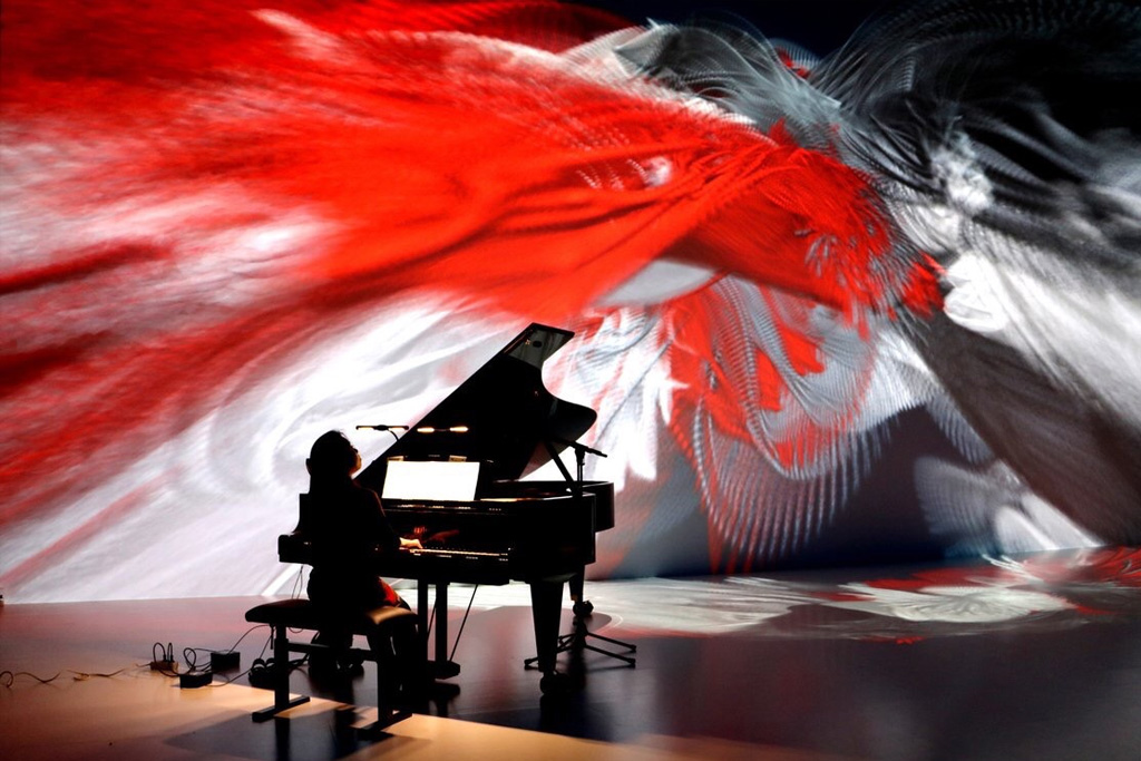 Pianist Maki Namekawa performing in front of a red and white animation.