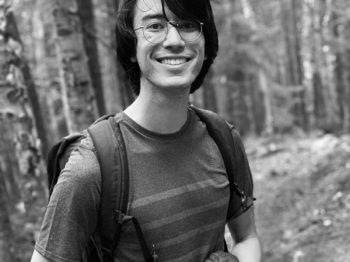 Jacob Geiger smiles at the camera while standing in a forest.
