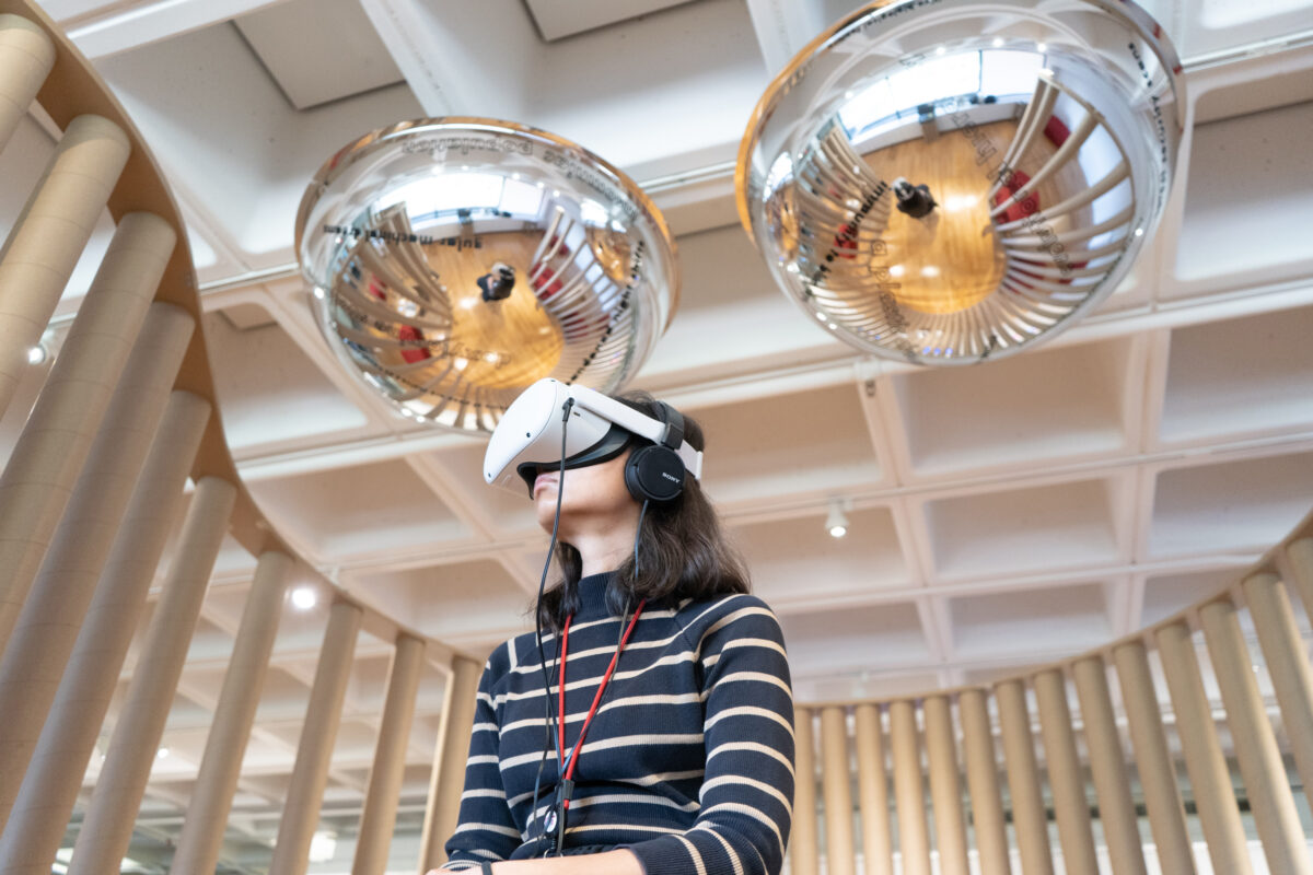 View looking up at a participant using a VR headset with two reflective domes hanging from on the ceiling above.