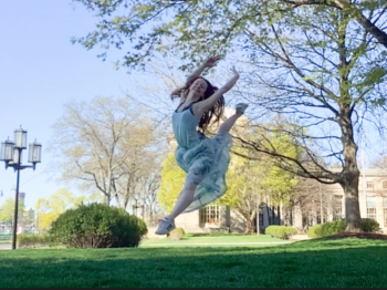 Elisabeth leaps in the air in a park with green grass.