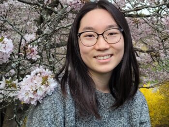 Sharon Jiang smiles at camera with a blossoming tree behind them.