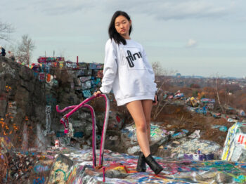 Sophia Chen stands forward with her arm holding her up near metal scraps in a landscape covered in graffiti art.