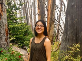 Teresa Gao stands facing the camera in a densely wooded area.