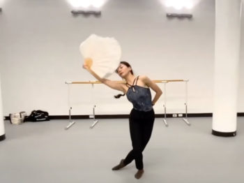 A dancer in a studio dancing with a white feathery fan.