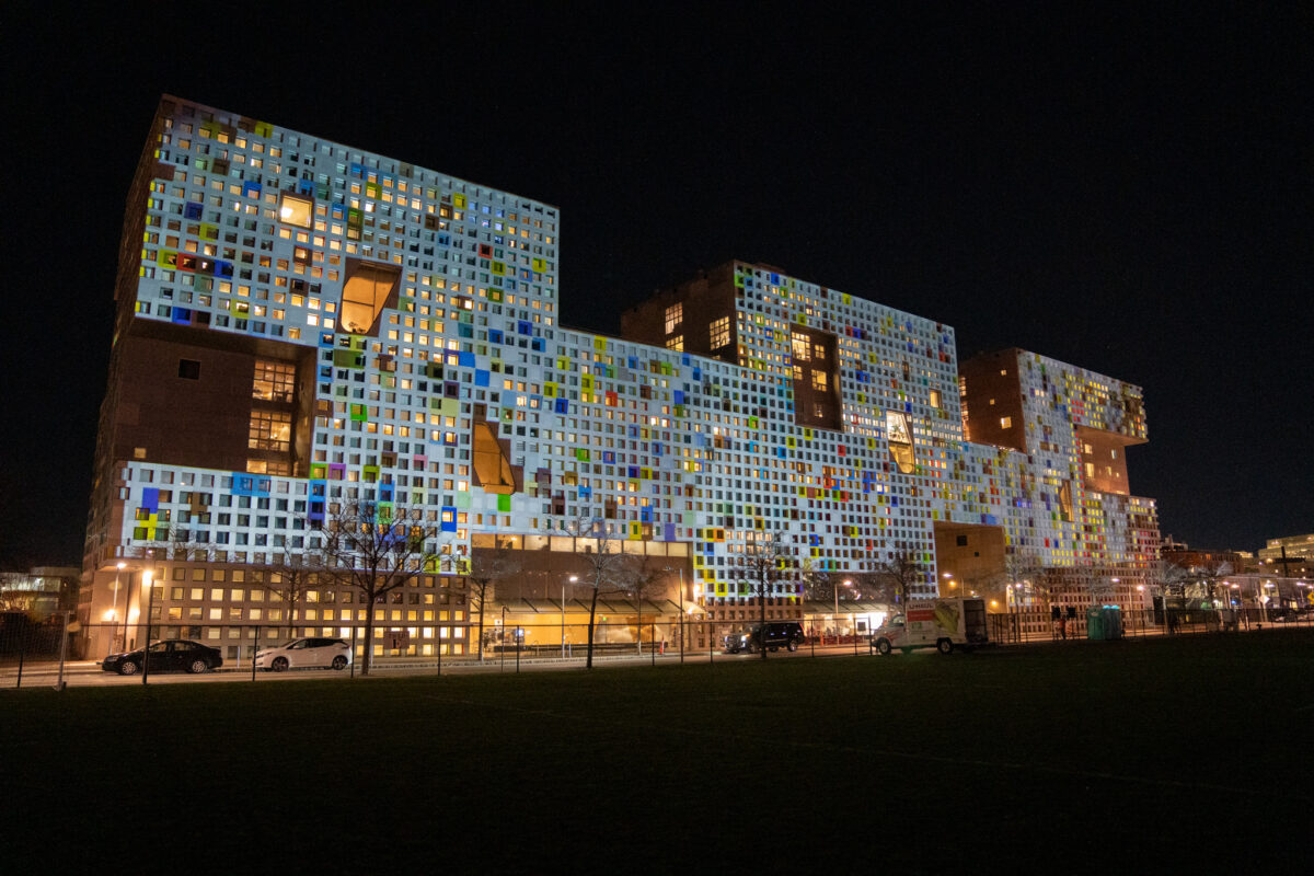 Side view of a grid-like building at night with a light display on the outside.