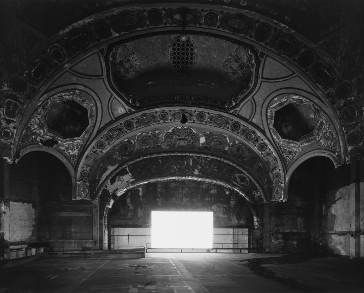 Black and white photograph of large room with decorative vaulted ceiling and a white square at the vanishing point. 