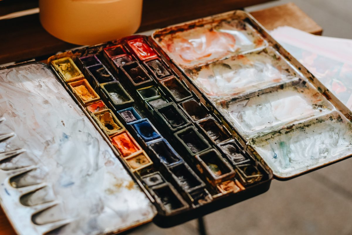 A set of cake watercolor paints sit in colorful rows within an open white case.