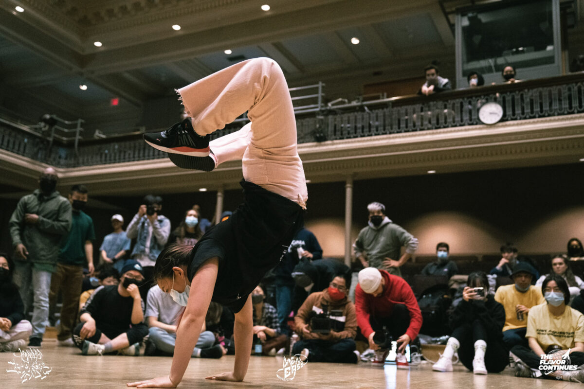 A dancer performs a handstand as other dancers watch.