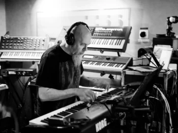 Jordan Rudess sits at a keyboard while wearing headphones.