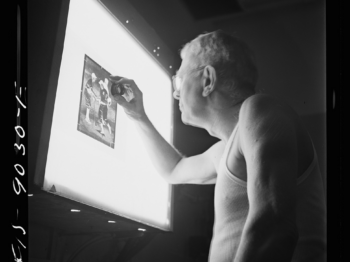 A person closely examining a black and white photograph suspended over a lightbox.