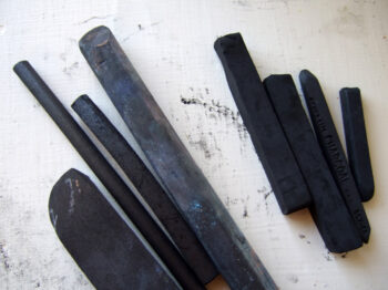 8 sticks of black charcoal arranged diagonally on a light background with minimal smudge marks.