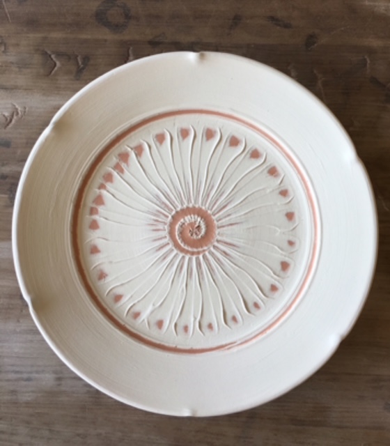 Overhead/looking down photograph of a clay plate with wavy surface design before the glaze firing.