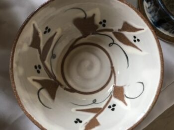 Overhead photograph of a glazed ceramic bowl with a vine, leaf and berry glaze pattern.