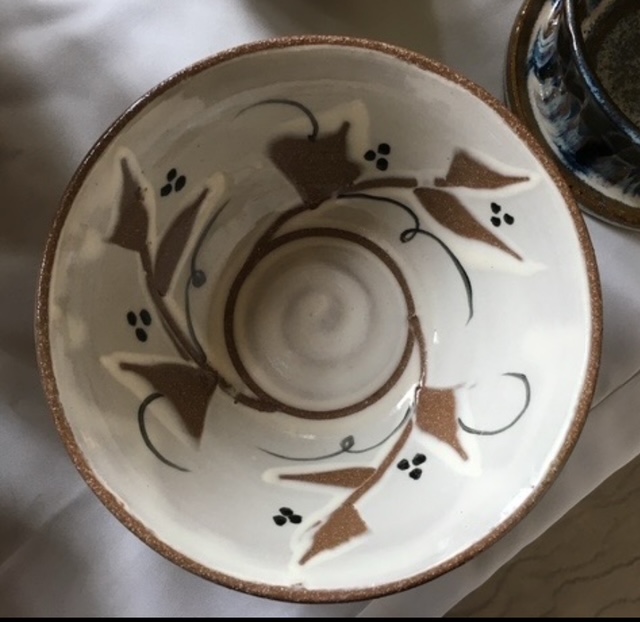 Overhead photograph of a glazed ceramic bowl with a vine, leaf and berry glaze pattern.