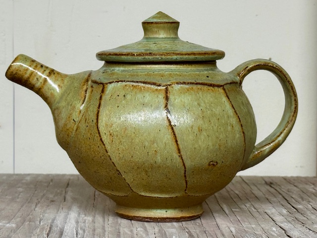 Green ceramic teapot sat on a wooden table with a white background.