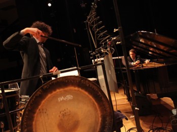 Two men perform piano and percussion in a concert.