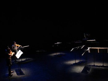 Two violinists perform on a dark stage.