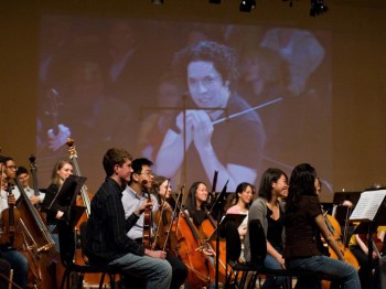 Projected image of an orchestra conductor behind a group of student orchestra musicians.