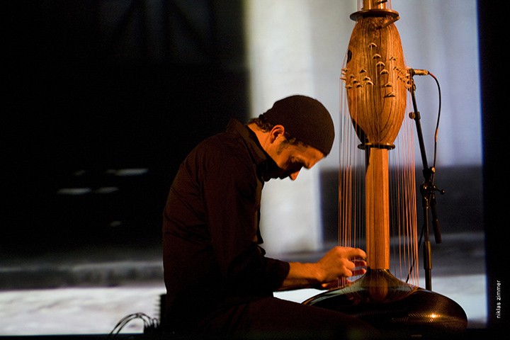 A man plucks strings on a large instrument made of wood and strings.