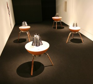 A gallery installation of sculptures made of stacked rings on tripod tables.