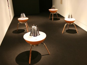 A gallery installation of sculptures made of stacked rings on tripod tables.