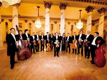 A group of musicians with string instruments poses for a photo in an ornate hall
